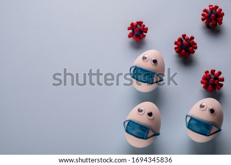 Eggs wearing medical mask for stop coronavirus and models of covid-19 virus on blue background. Epidemic coronavirus COVID-19 concept. Place fo text Royalty-Free Stock Photo #1694345836