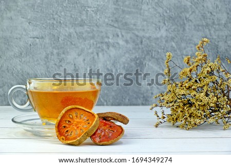 Bael fruit juice herbal drink surrounded by pieces of dried bael fruit on white wooden table with concrete background.