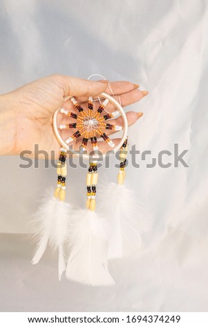 Dream catcher in female woman hand on satin, handmade native american of yellow blue beads with white feathers. Bad dreams protection. Concept peaceful, peace of mind, meditation, tranquility