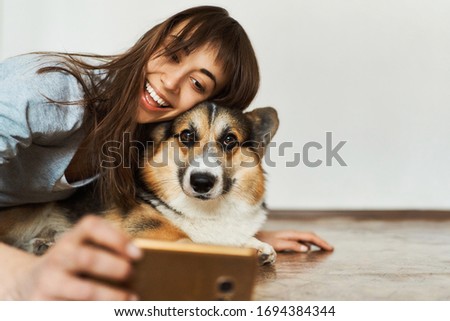 Portrait laughting young woman hugging cute Welsh Corgi dog dog and taking selfie with pet on smartphone camera. Concept stay at home, friendship with dog, taking picture.