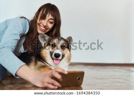 joyful smiling young woman hugging cute Welsh Corgi dog dog and taking selfie with pet on smartphone camera. Concept stay at home, friendship with dog, taking picture.