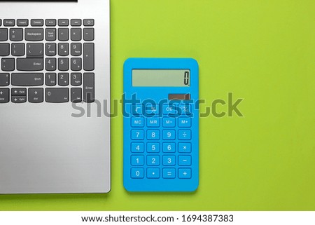 Calculator and laptop on green background. Top view