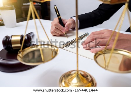 justice and law concept.Male judge in a courtroom with the gavel,working with,digital tablet computer docking keyboard,eyeglasses,on wood table warm colours sun light.
