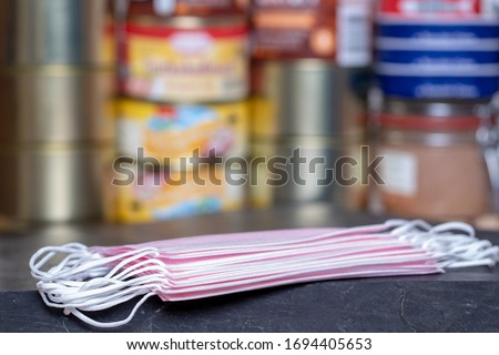 Coronavirus panic concept. Focus on stack of surgical masks on table over a pile of canned foods with a long shelf life such as fish, vegetables and meat stew and other goods. 