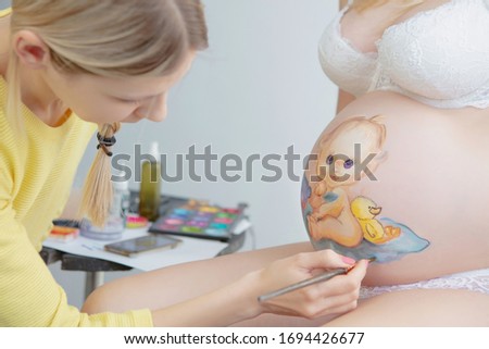 Makeup artist draw a small toddler on the belly of a pregnant young woman