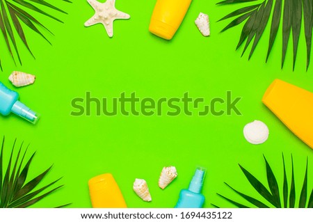 Sun protection Summer background vacation travel concept Yellow blue bottles of sunscreen cream tropical palm leaves shells starfish on green background top view flat lay copy space. Summer cosmetics