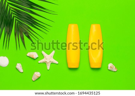 Sun protection. Summer background vacation travel concept Yellow bottles of sunscreen cream, tropical palm leaves, shells, starfish on green background top view flat lay copy space. Summer cosmetics