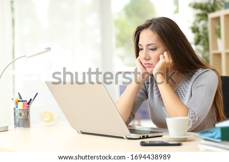 Bored entrepreneur woman looking at laptop screen sitting on a desk at home Royalty-Free Stock Photo #1694438989