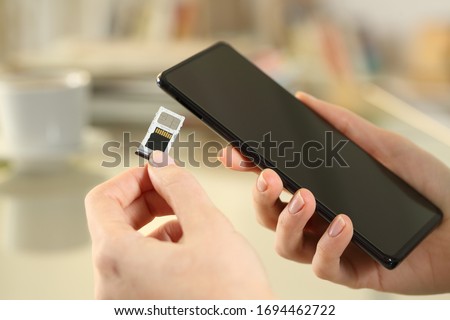 Close up of girl hand inserting sim and sd card on smart phone sitting on a desk at home Royalty-Free Stock Photo #1694462722