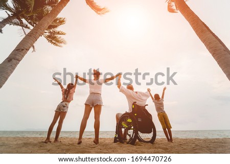 Disabled man in a wheelchair with his family on the beach. Silhouettes at sunset