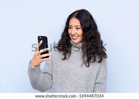 Spanish Chinese woman over isolated blue background making a selfie
