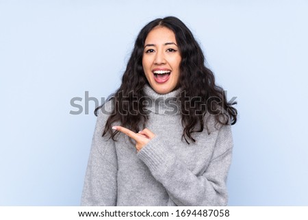 Spanish Chinese woman over isolated blue background surprised and pointing side