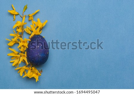 Blue easter egg with yellow flowers on a blue background. Top view. Flatlay. Object on the left side of the photo