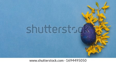 Blue easter egg with yellow flowers on a blue background. Top view. Flatlay. Object on the right side of the photo