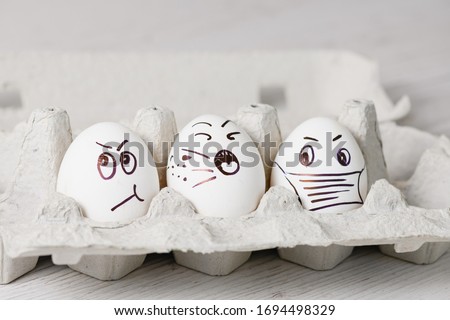 Painted by marker white eggs with funny emotional faces close up in paper tray for spring holiday during epidemic coronavirus.