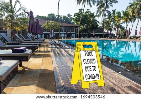 ''Pool closed due to COVID-19'' sign against a luxury hotel pool