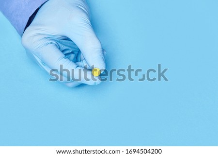 doctor holds one yellow pill in his hand. blue background