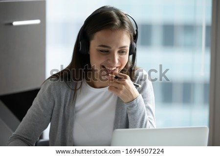 Happy millennial female in headphones watch webinar on laptop in modern office, smiling young businesswoman have fun laugh talk on video call with client or colleague use wireless Internet connection Royalty-Free Stock Photo #1694507224