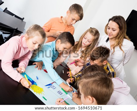 Smiling team of elementary age children and female teacher drawing on one sheet