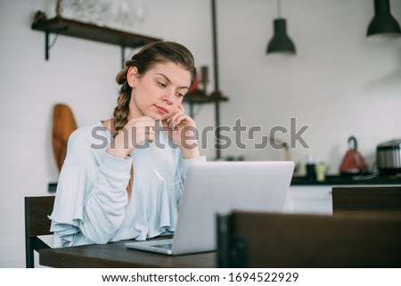 A woman sits in the living room with a laptop, looks at the screen, takes notes, learns a foreign language, reads an online training course, education on the Internet, consults with a client on video