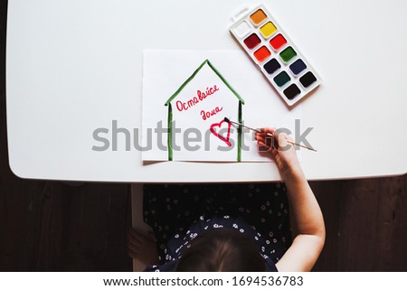 child draws watercolors at a white table drawing - a house with the words stay home in Russian