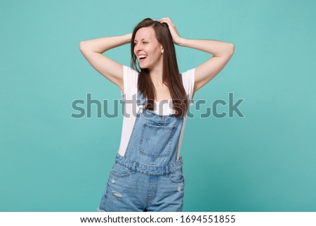 Stunning cheerful young brunette woman girl in casual denim clothes posing isolated on blue turquoise wall background. People lifestyle concept. Mock up copy space. Put hands on head, looking aside