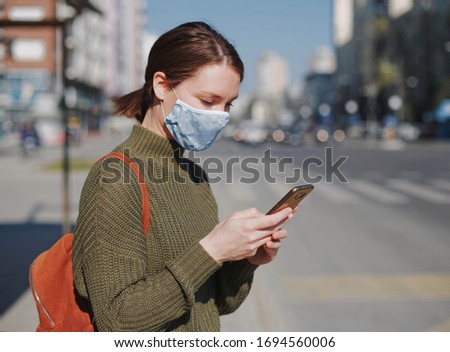 Young woman using smart phone in the city wearing face mask protection for virus coronavirus covid 19 Royalty-Free Stock Photo #1694560006