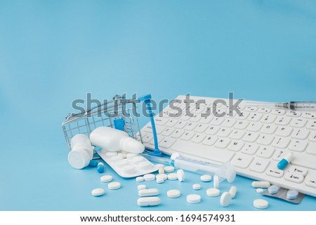Shopping cart toy with medicaments and Keyboard. Pills, blister packs, medical bottles, thermometer, protective mask on a blue background. . Health care and internet shopping. Top view with place for