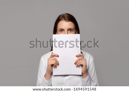 young businesswoman in white shirt with papers near face isolated on grey