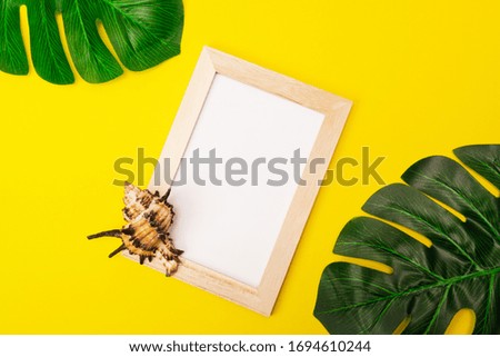 tropical mock up with white photo frame and palm leaves on colorful yellow background. Photo frame with empty place for text or advertisement with seashells on a yellow background