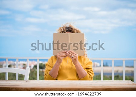 Unrecognizable woman read a paper book outdoor with wooden table in front of her and blue beautiful sky in background - concept of reading and studying for people Royalty-Free Stock Photo #1694622739