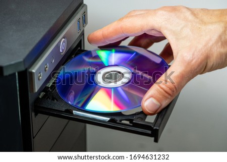 Hand inserting DVD into a computer. Closeup. Royalty-Free Stock Photo #1694631232