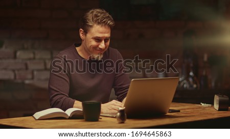 Older man tele working with laptop computer at home office in dark room, thinking, looking busy. Royalty-Free Stock Photo #1694645863