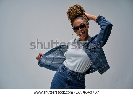 Woman with wide opened smile with bun of braids in earrings in sunglasses posing