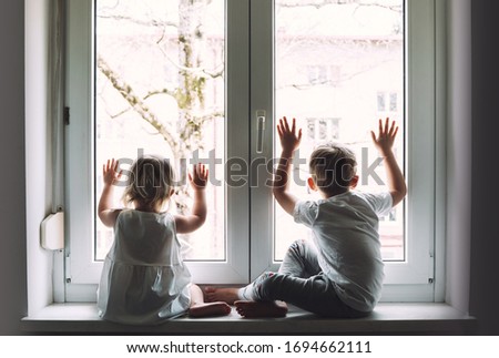 Little children are at home in quarantine and look out the window. Photo of kids leisure at home. Photo concept of social, disease, illness, quarantine Pandemic Coronavirus Covid-19
