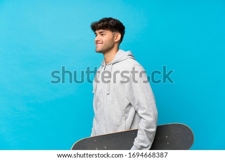 Young handsome man over isolated blue background with skate