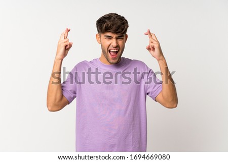 Young handsome man over isolated white background with fingers crossing