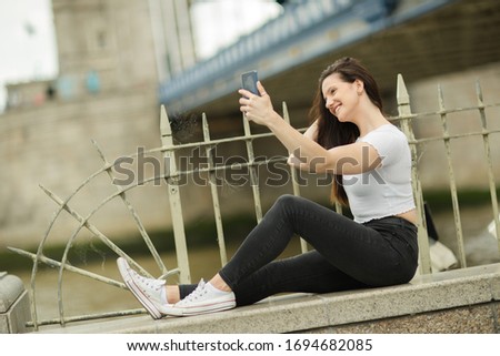young woman sitting on a wwall taking a selfie