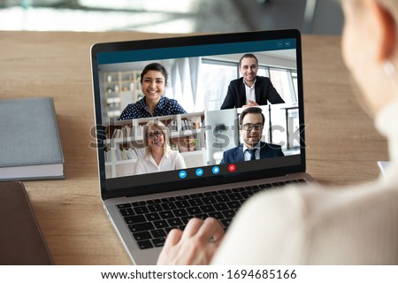 View over female shoulder at computer webcam screen view of four different age and ethnicity business people negotiating distantly using video conference app, video call virtual communication concept Royalty-Free Stock Photo #1694685166