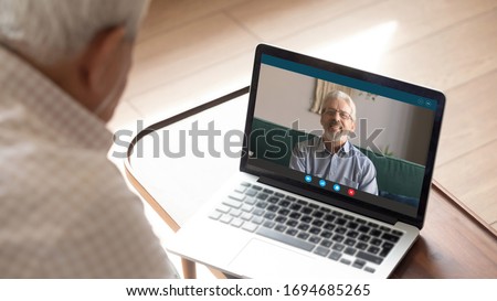 80s old man sit indoor look at pc screen talk with 50s male friend by video call. Multi-generational relatives communicating use modern tech internet connection laptop and videoconference application Royalty-Free Stock Photo #1694685265