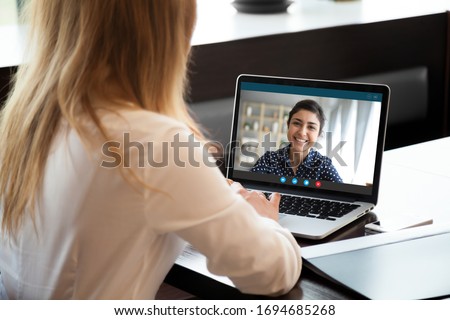Laptop screen view over female shoulder, businesswomen working from home on common project, company representative and client communication. Diverse girls friends chat via video conference application Royalty-Free Stock Photo #1694685268