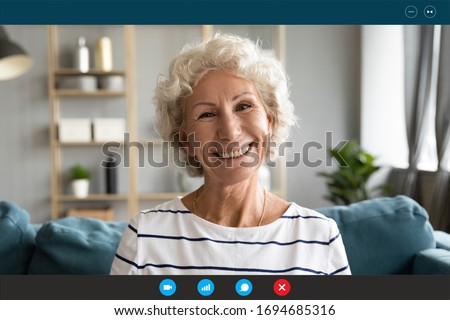 Head shot old granny sit on couch smiles looks at webcam enjoy pleasant distant conversation via pc and videoconference app, online consultation with doctor, chat with relatives adult children concept Royalty-Free Stock Photo #1694685316