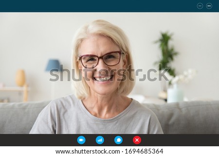 Pc screen view head shot 50s woman wear glasses looking at webcam seated on sofa at home chatting with adult children relatives friends by video conference app. Communication online video call concept Royalty-Free Stock Photo #1694685364