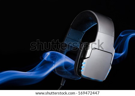 Silver large headphones with stream of blue smoke. Single object on black background.