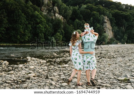 Mom, dad hugging daughter walking on stone near lake. The concept of summer holiday. Mother's, father's, baby's day. Family spending time together on nature. Family look. Sun light. Back view.