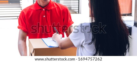 Young courier delivery man in red uniform holding a parcel cardboard box delivering package and woman putting signature in clipboard to receiving package at home.online shopping and transport cargo