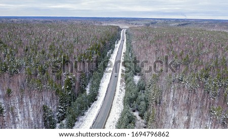 A blue car rides along a winter asphalt road in the forest. Snow on trees and roadsides, Aerial View  