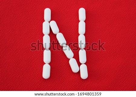 Alphabet made of pills on a red background. Abc from drugs. 
Letter N made from pills. Capital letter N of medicines