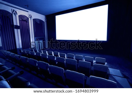 Cinema theater screen in front of seat rows in movie theater showing white screen projected from cinematograph. The cinema theater is decorated in classical style for luxury feeling of movie watching. Royalty-Free Stock Photo #1694803999
