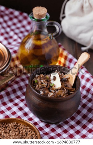 Traditional russian meal: cooked buckwheat porridge with brown butter in clay pot, served with butter, fried mushrooms, onion. Healthy food, low calories. Copper pan, wooden background, close up